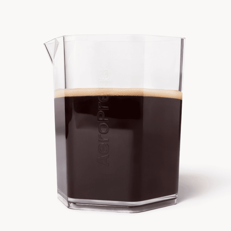 Jarra hexagonal transparente de AeroPress llena de café oscuro con una fina capa de espuma.