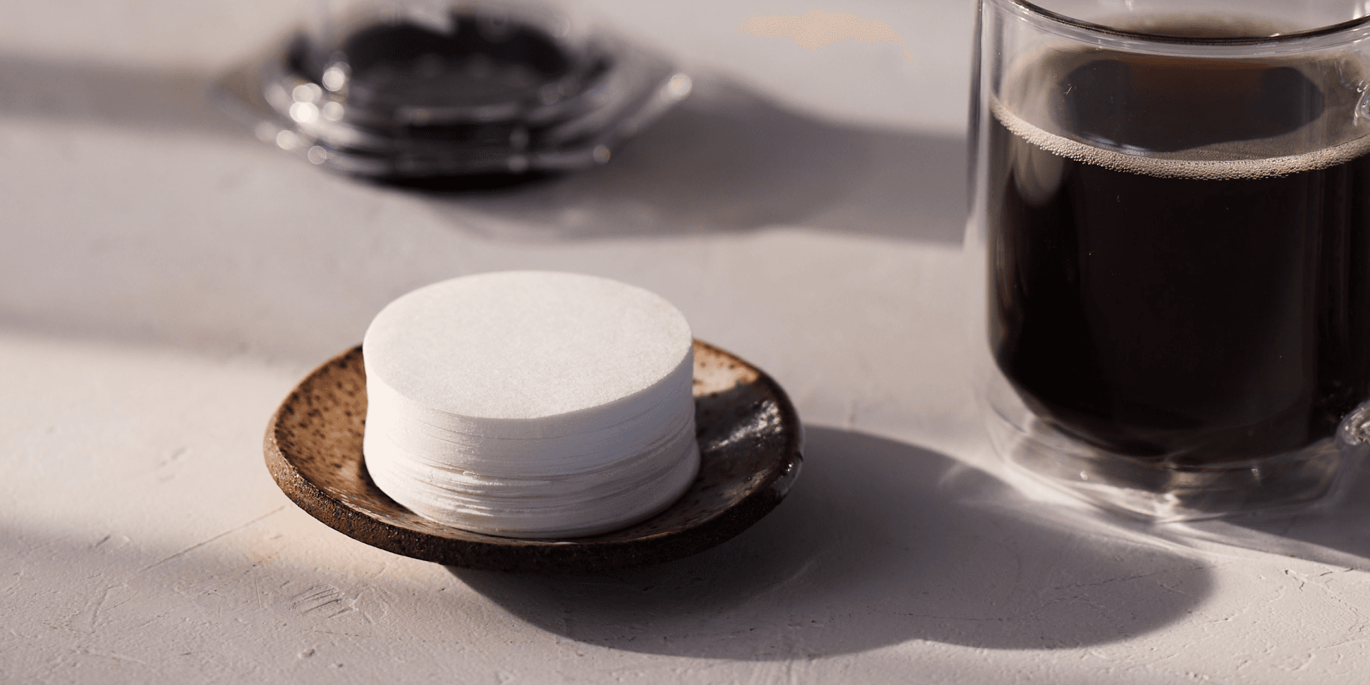 Pila de filtros redondos sobre un plato pequeño junto a una taza de café negro.