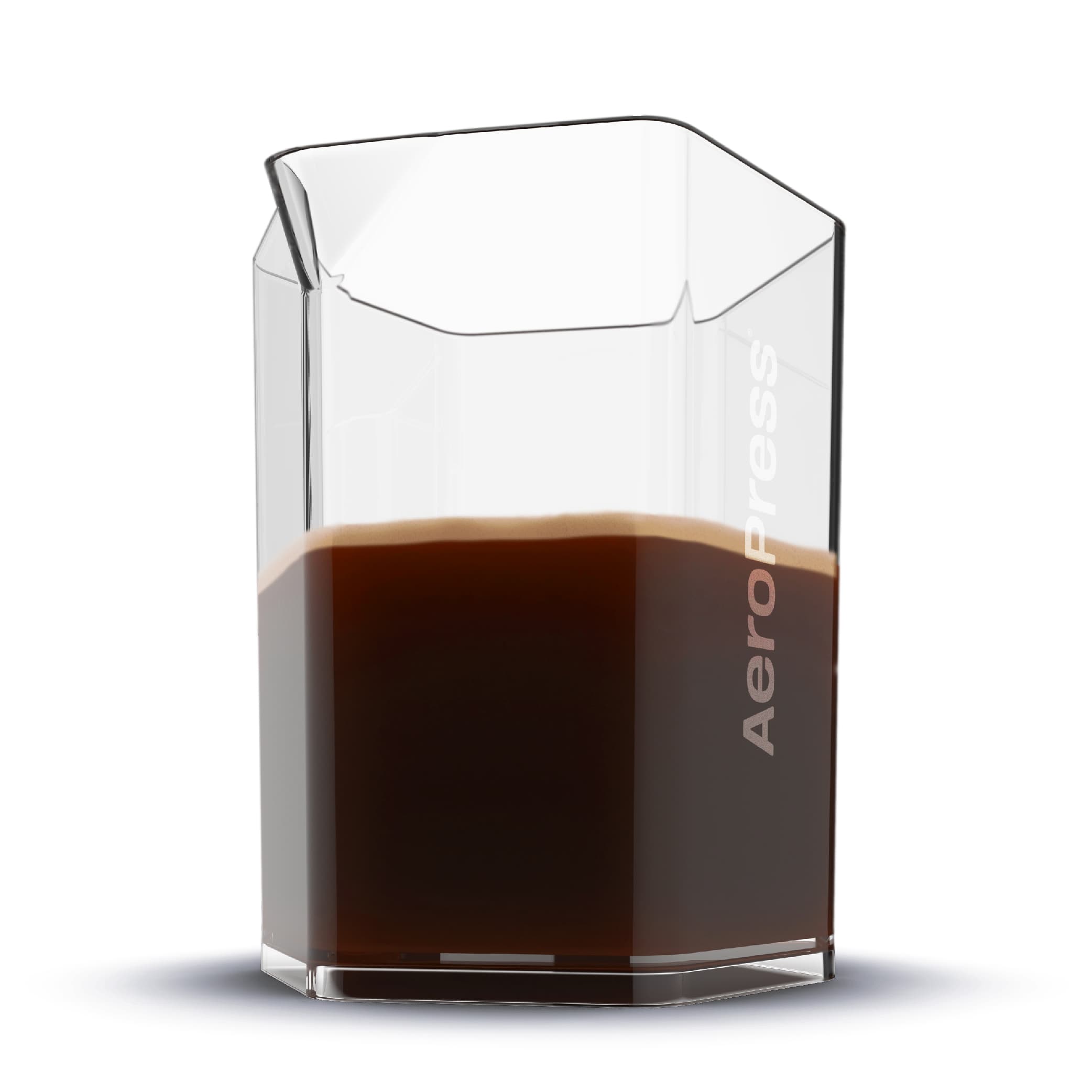 Jarra hexagonal de vidrio AeroPress medio llena de café oscuro con espuma sobre fondo blanco.