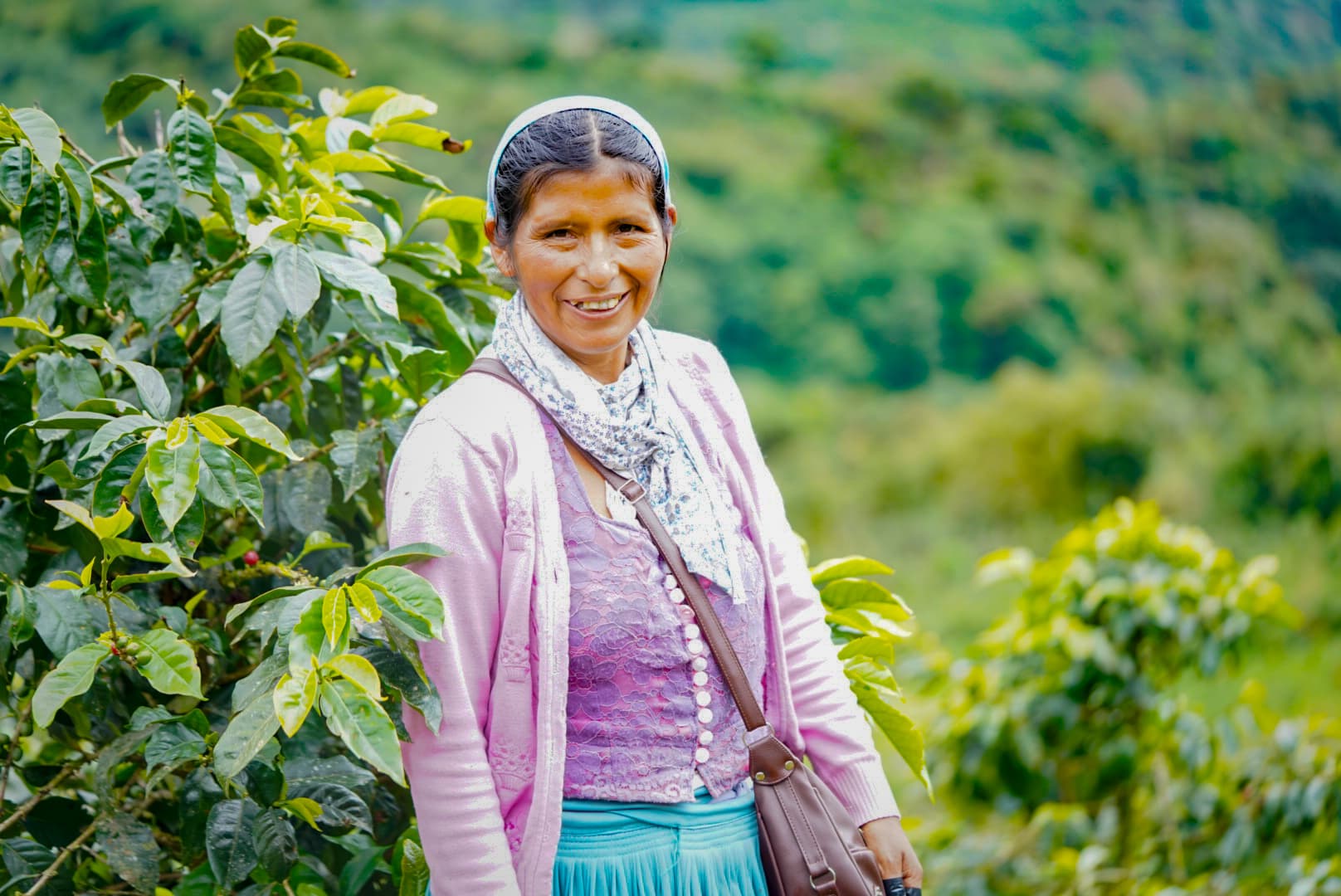 Mujer sonriente con vestimenta colorida posa en una plantación de café verde y exuberante.