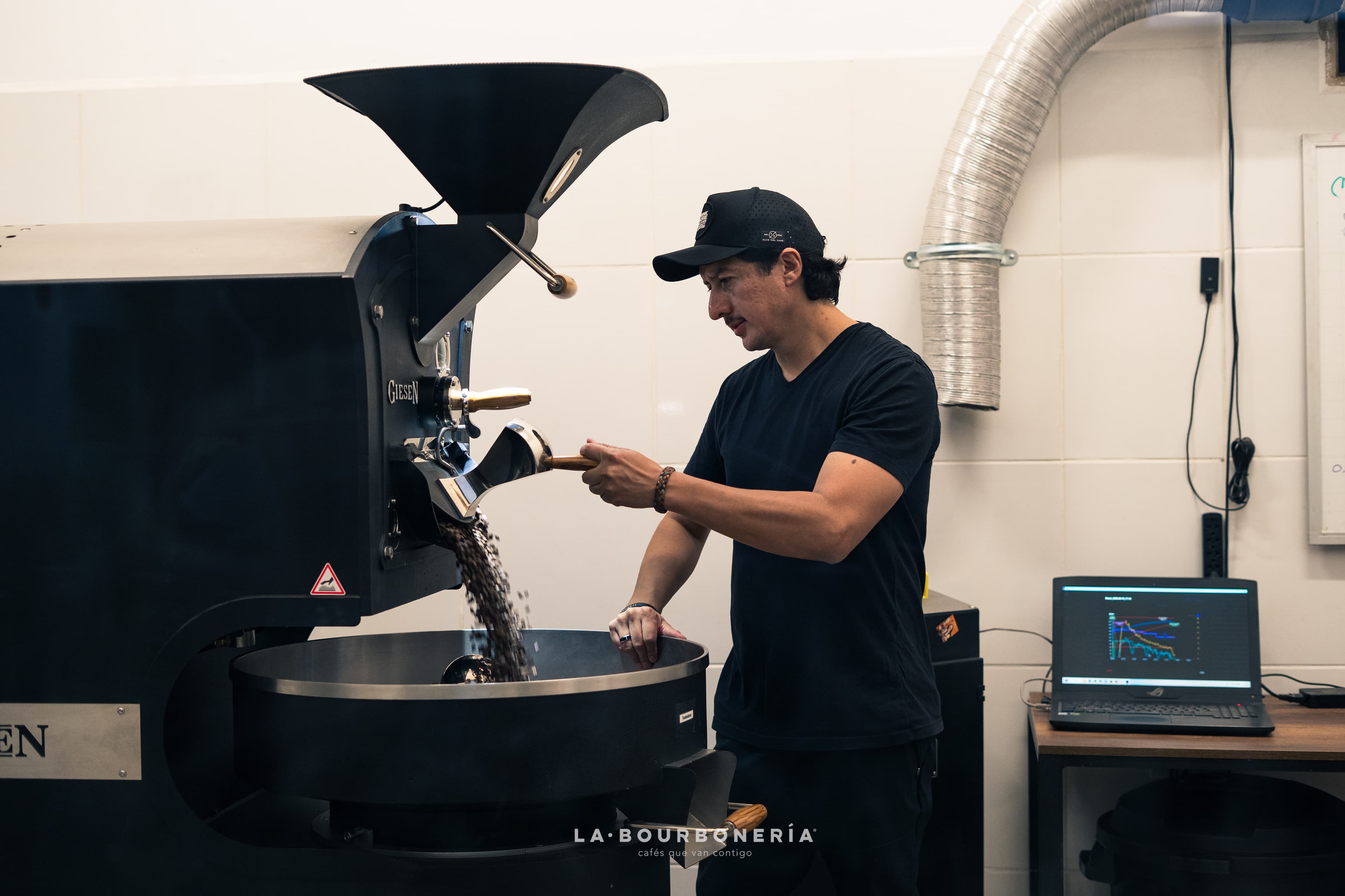 Hombre operando una máquina tostadora de café profesional mientras los granos caen al enfriador.