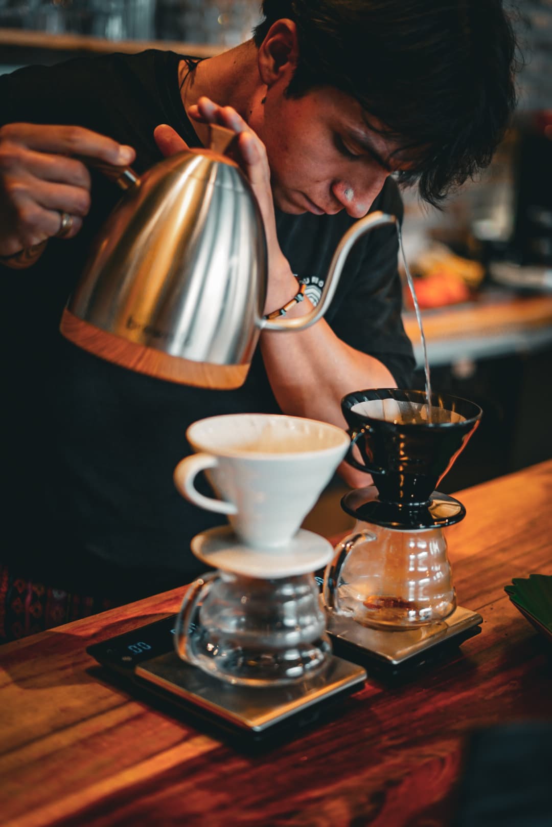 Barista vertiendo agua con precisión desde una tetera de cuello de cisne sobre café.