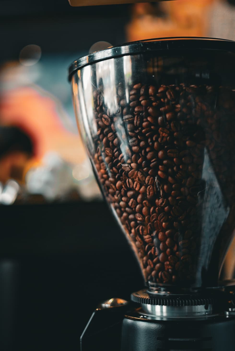 Tolva transparente llena de granos de café tostados oscuros en un molinillo de café profesional.