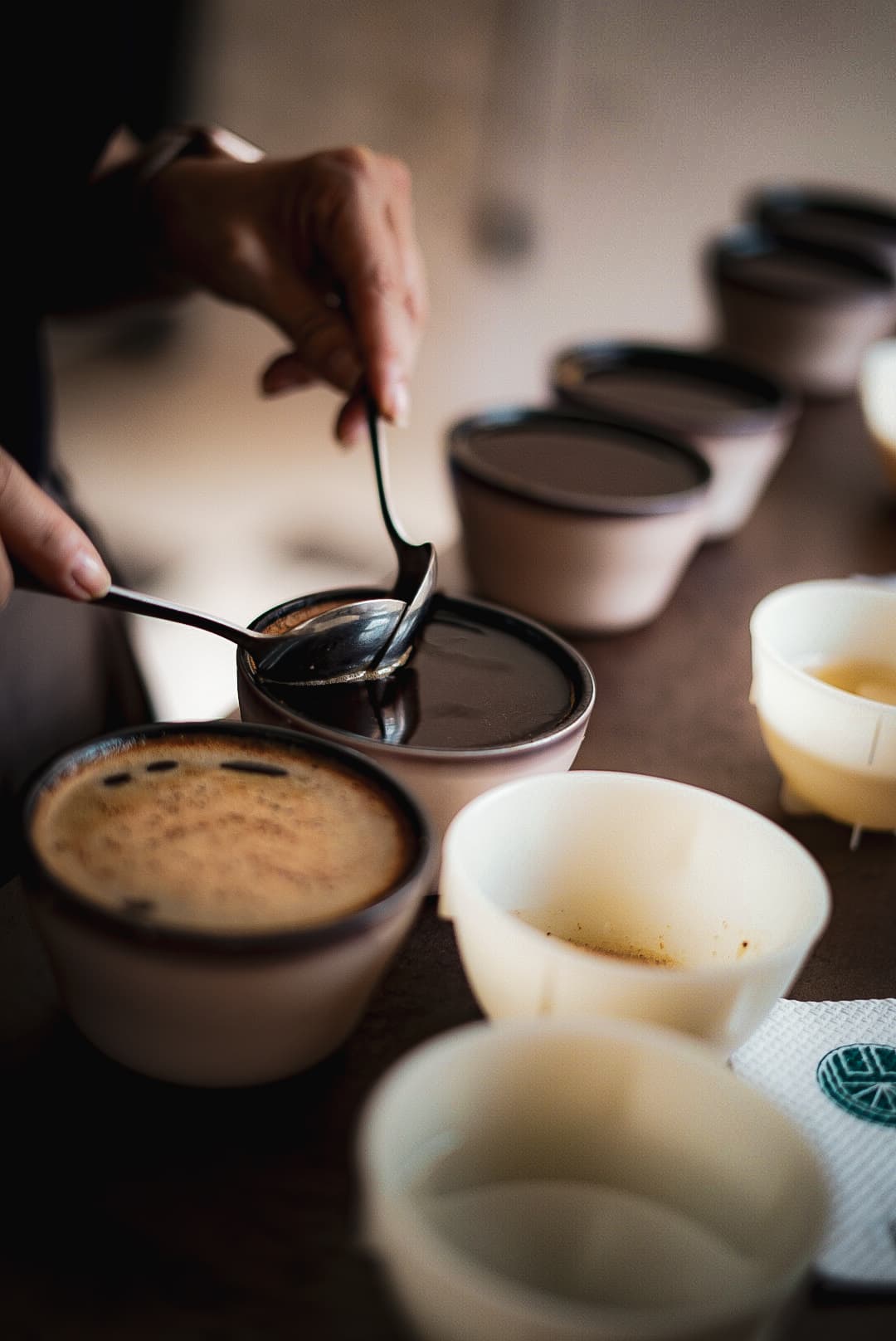 Manos usando cucharas para catar café en cuencos alineados durante una sesión de catación profesional.