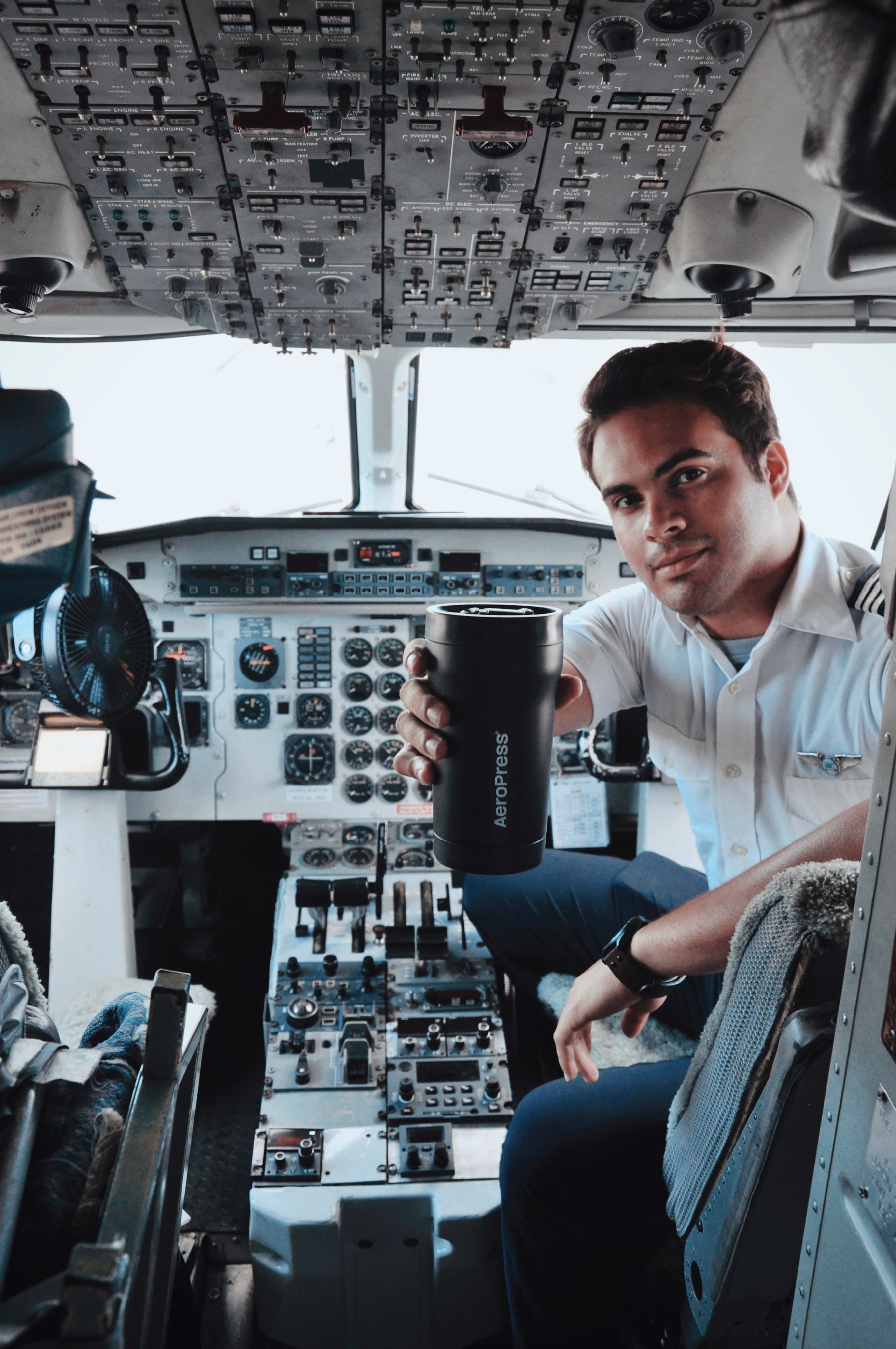 Piloto en la cabina de un avión sosteniendo un termo negro de viaje AeroPress.