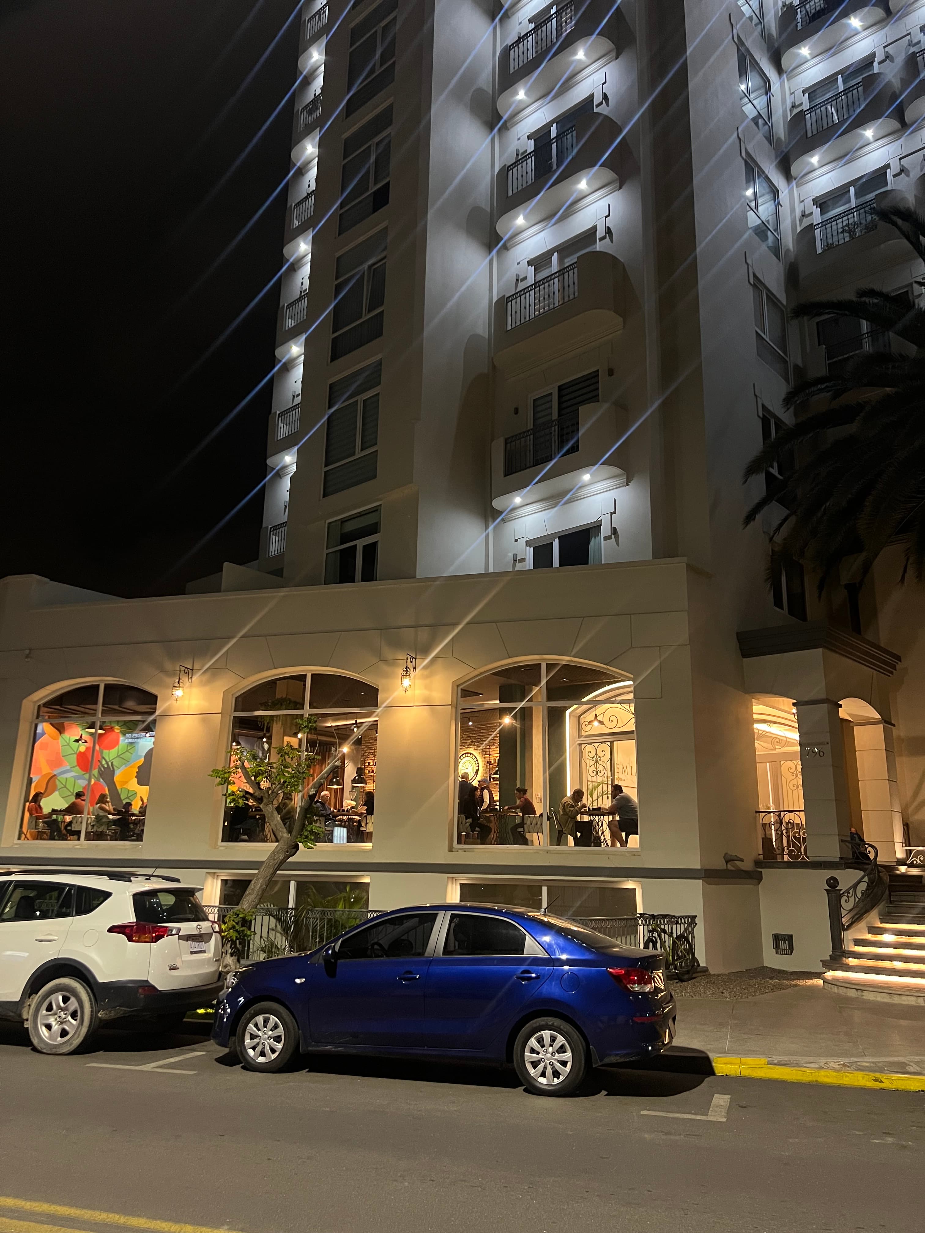 Edificio blanco con restaurante de ventanales arqueados y coches estacionados en la calle de noche.
