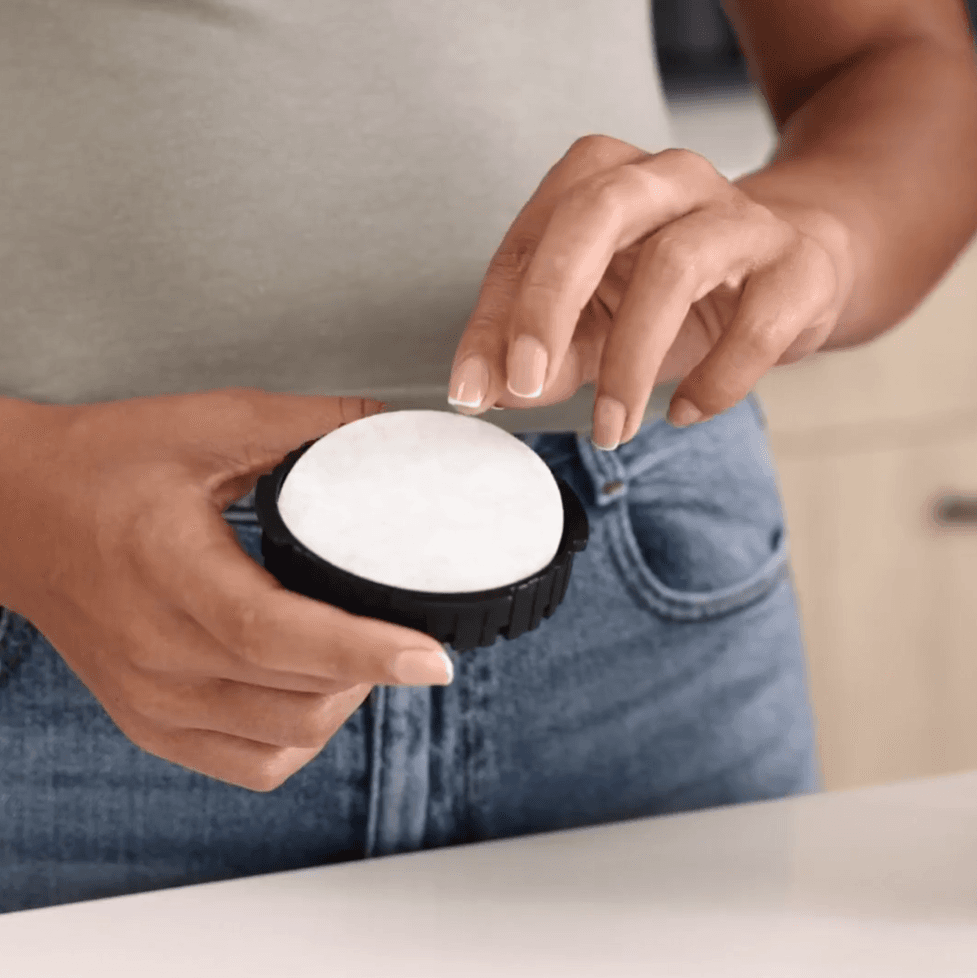 Manos de una persona sosteniendo un objeto circular negro con una almohadilla blanca redonda.