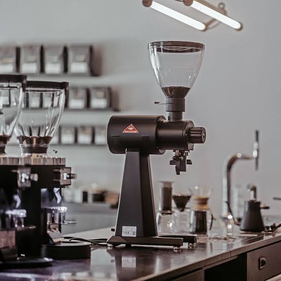 Molinillo de café profesional negro sobre un mostrador en una cafetería moderna y bien iluminada.